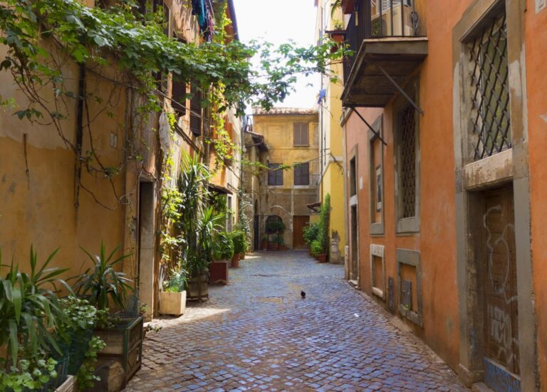 A picturesque alley located in the Trastevere neighborhood of Rome, which is known for its narrow, cobblestone streets and features traditional architecture with terracotta-colored buildings.
