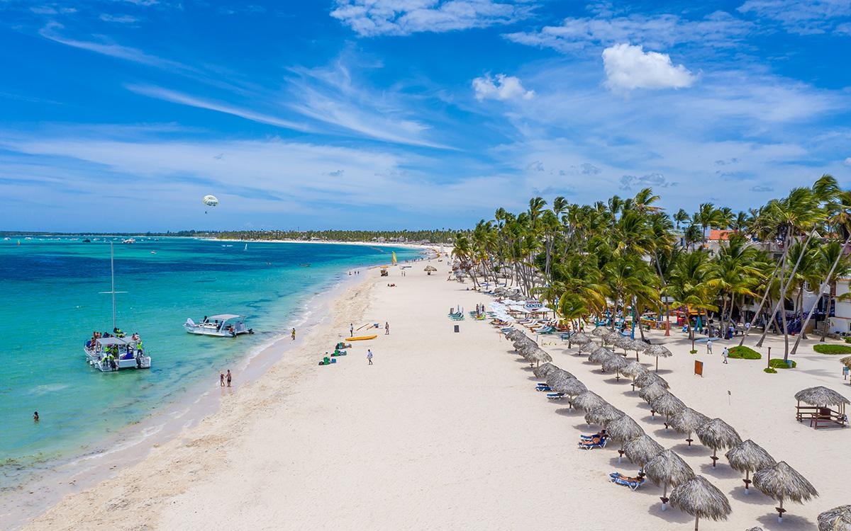 The white sands of Bavaro Beach in Punta Cana, Dominican Republic lined with palapas and palm trees.