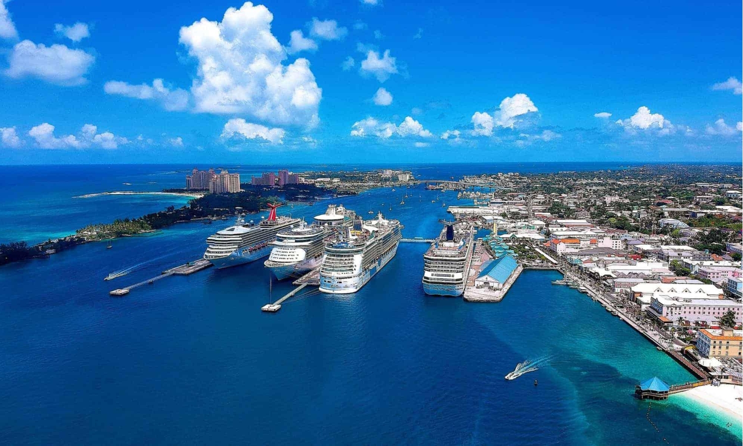 Nassau Cruise Port in the Bahamas, bustling with multiple large cruise ships docked simultaneously vith views of the cruise piers along the downtown waterfront and Paradise Island in the background.