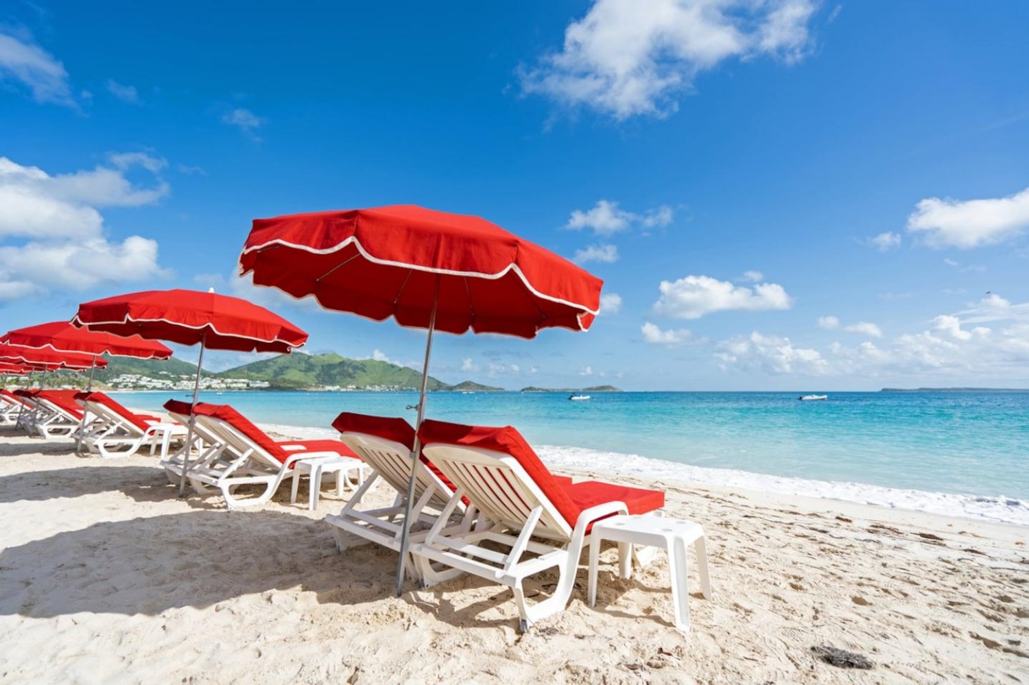 Red beach umbrellas and loungers lined up along the sandy shores of Orient Bay in Saint Martin.