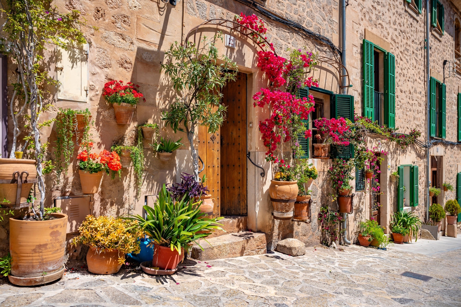 A traditional stone building in Valldemossa, Mallorca, decorated with potted bougainvillea and other plants.